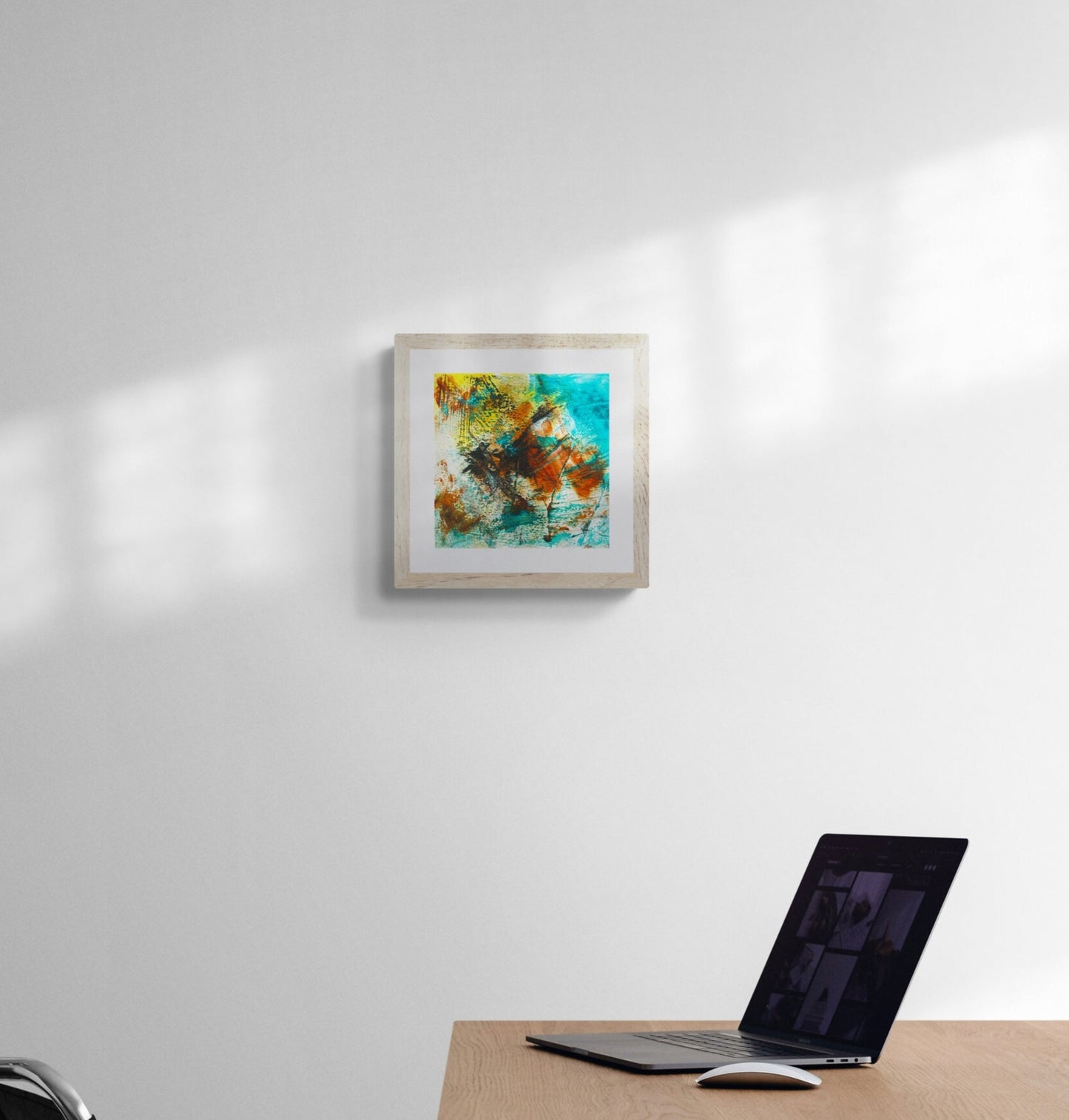 Modern office setup with a desk, chair, and framed abstract painting on a white wall.
