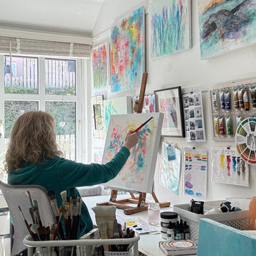 Person painting in a studio with colorful artworks on the wall