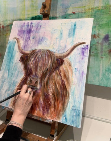 painting a highland cow on an easel with a colorful background