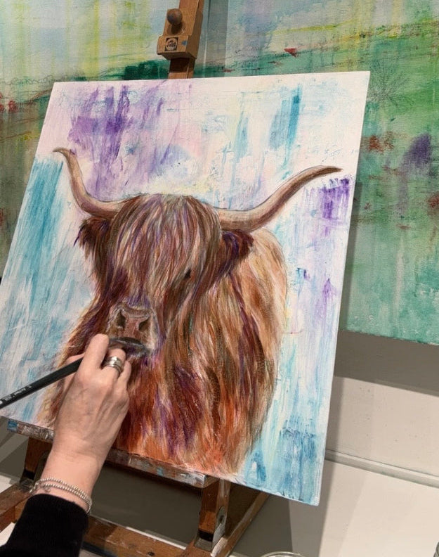 painting a highland cow on an easel with a colorful background