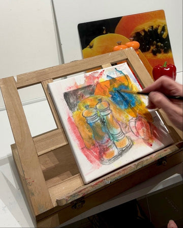 painting a still life scene on a canvas with a wooden easel.