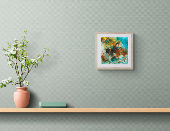 Framed abstract painting on a wall above a wooden shelf with a vase and plant.
